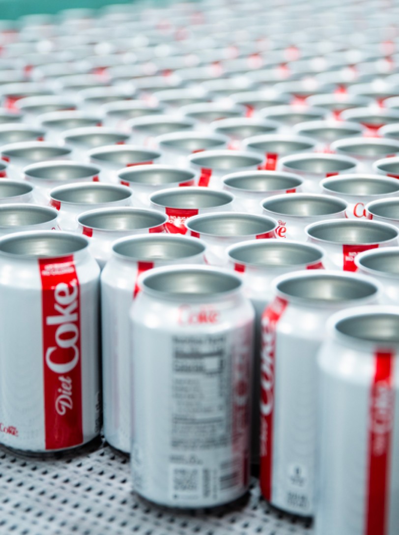 Cans of Diet Coke are lined up on a conveyor belt.