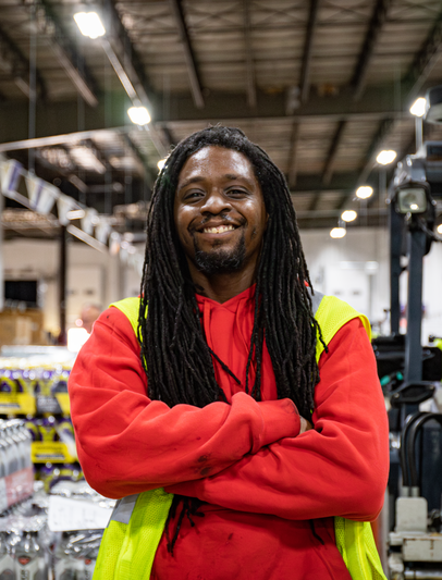 Man smiles in safety vest standing in front of warehouse pallets