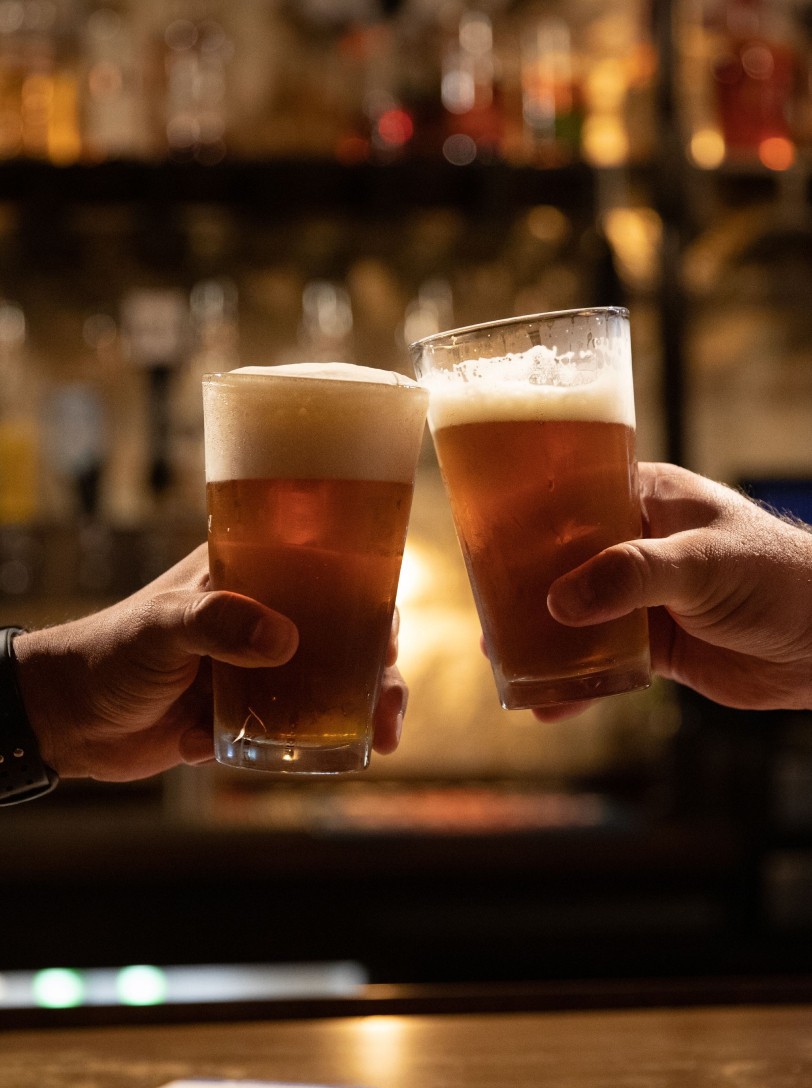 Two people toasting a beer in front of a bar