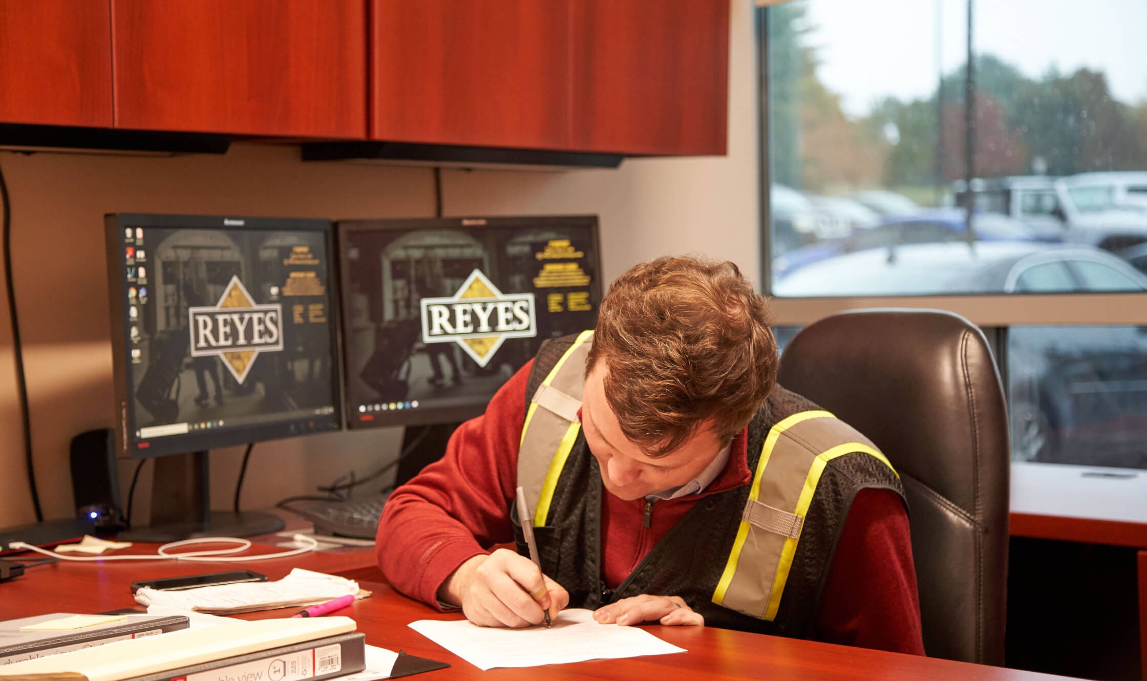 Reyes Beer Division employee sitting in office, writing on paper with monitors behind them