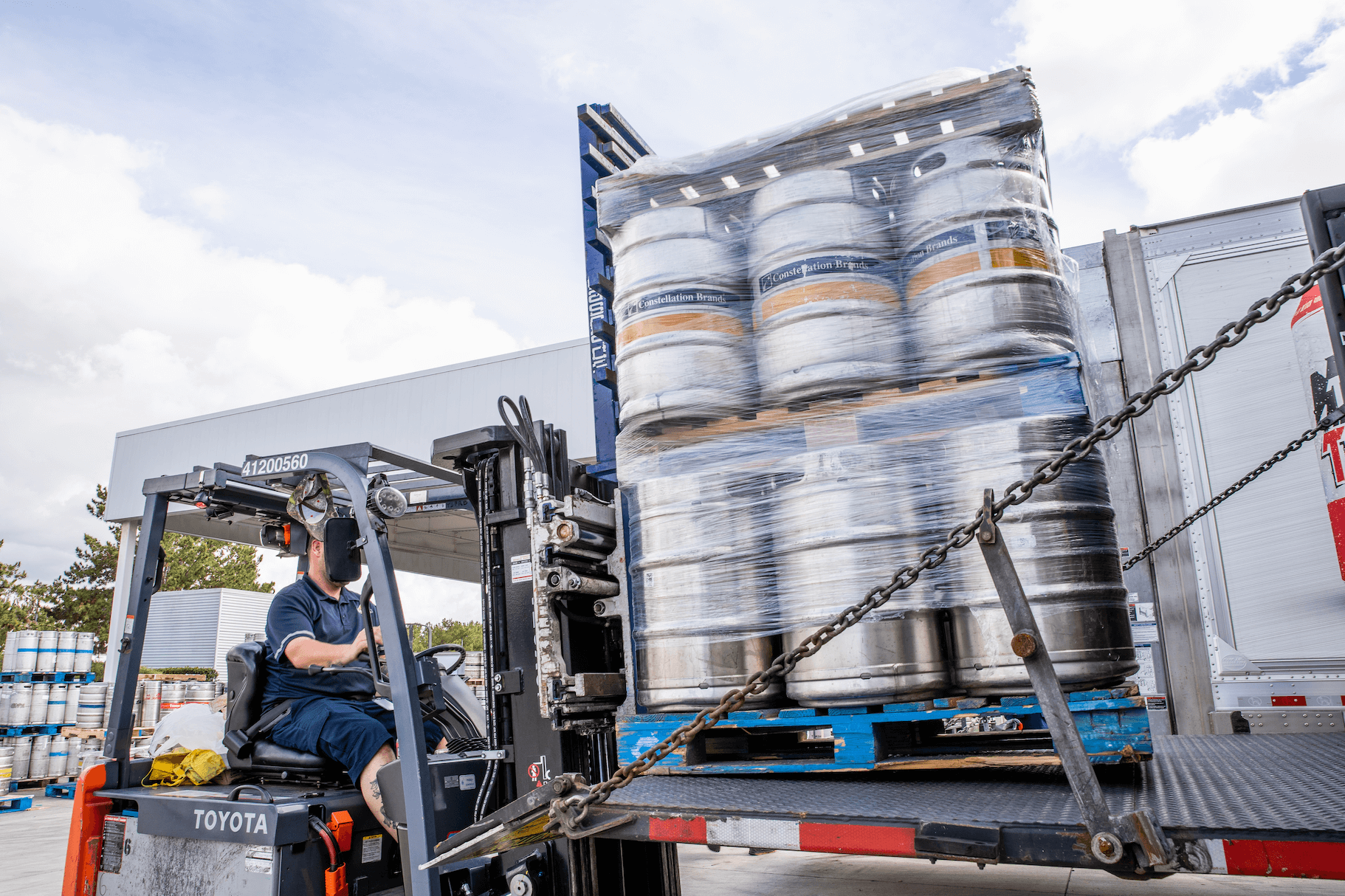 Forklift operator moving pallets of kegs of beer onto back of truck