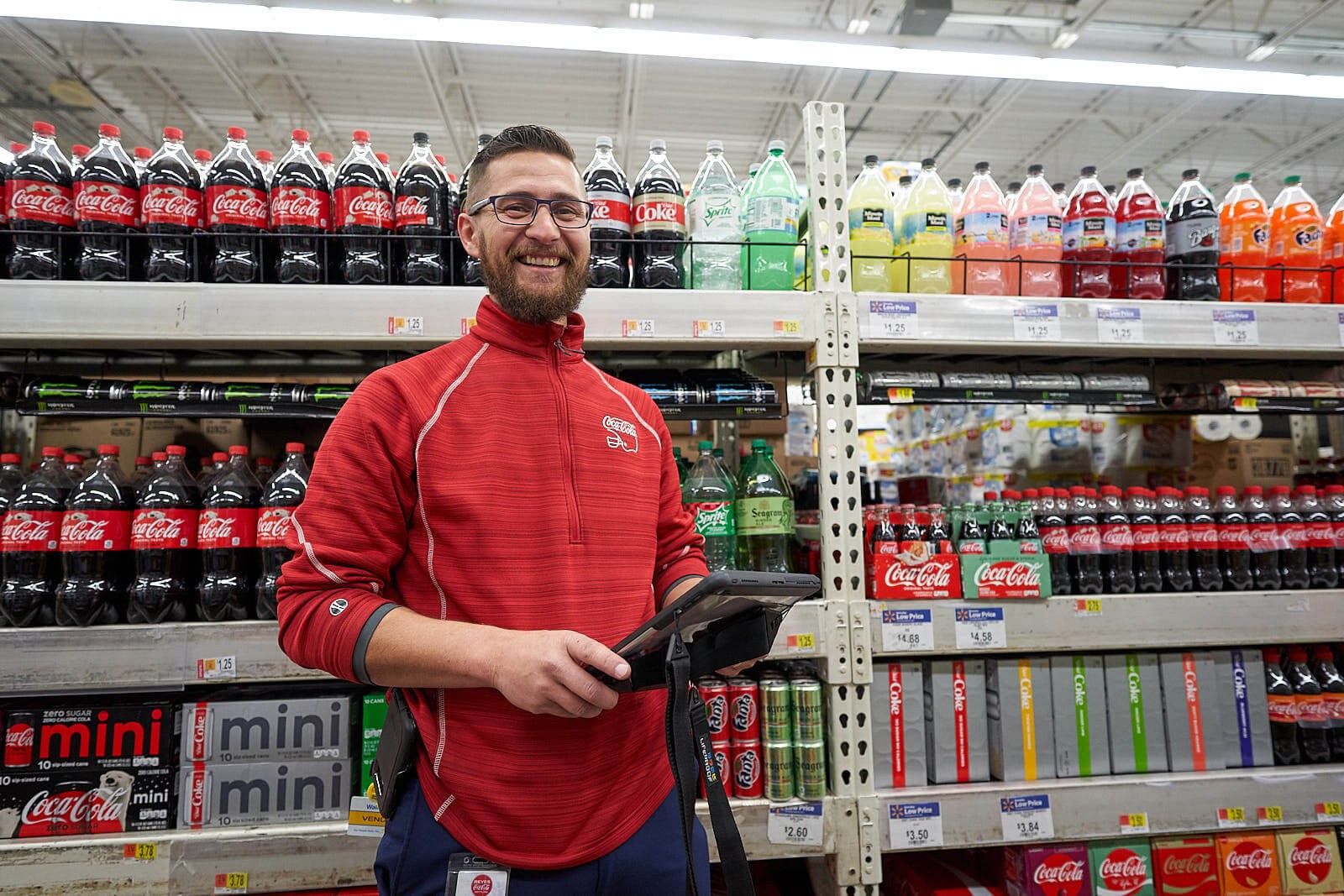 Smiling man stands by case of Coca-Cola products in grocery store