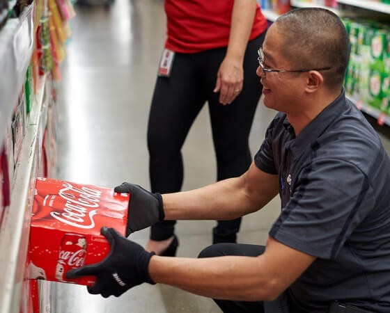 Smiling man wearing gloves and puts a Coca-Cola box on the shelf