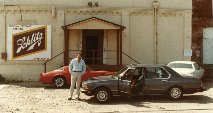 Duke Reyes stands in front of building in 1976 with vintage car door open